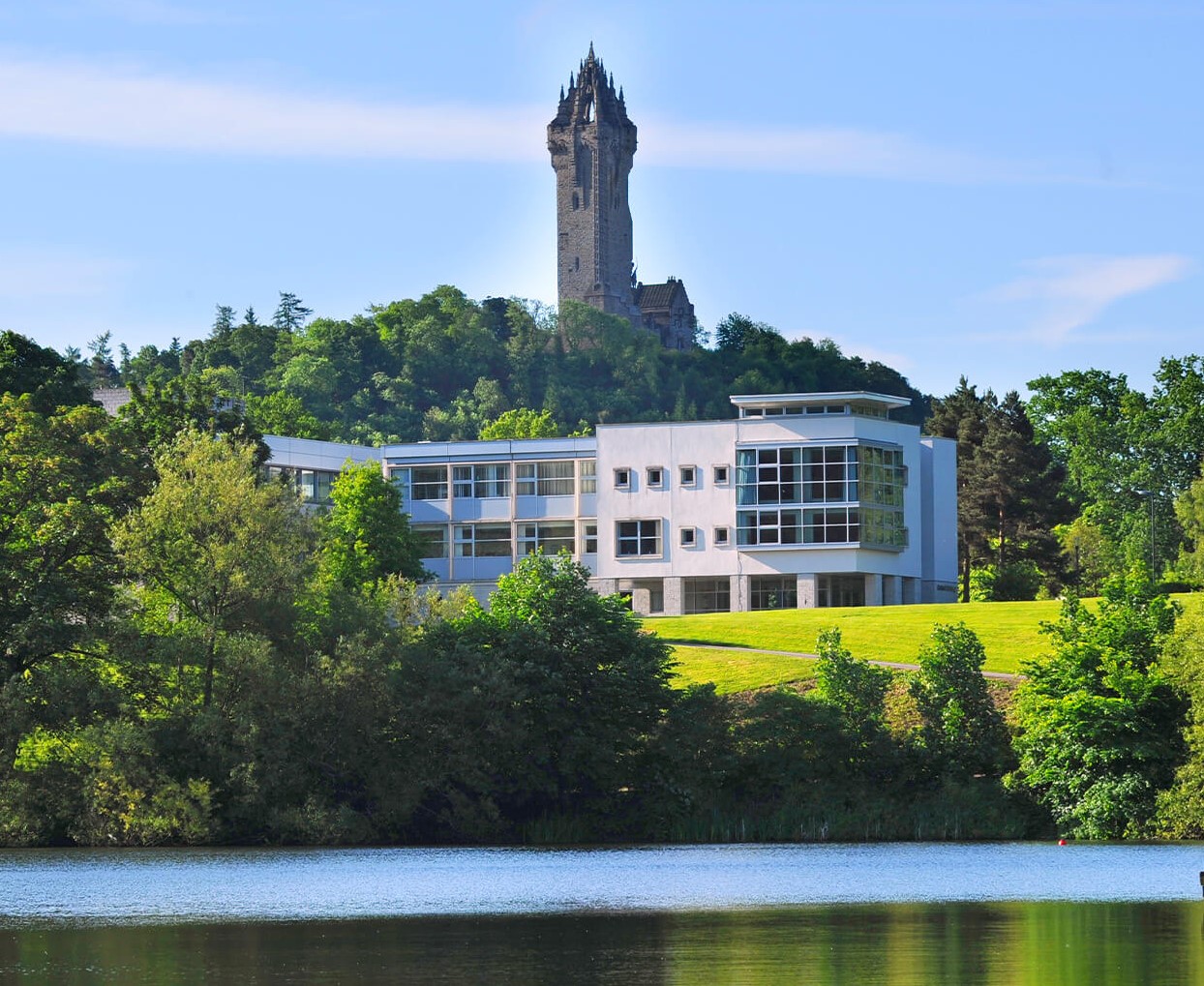 Image of Stirling University campus - very green and leafy with a white building in front of the historic Wallace monument